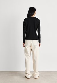 Black long-sleeve shirt, fitted at the waist, paired with loose, cream-colored jeans with blue stitching on the back pockets.