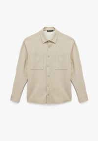 Camisa de botones color beige claro con cuello, dos bolsillos frontales, mangas largas y una tela lisa y texturizada.