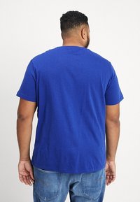 Kortärmad t-shirt med rund hals i livfull blå bomull. Har en avslappnad passform och en slät textur; bakifrån visas en enkel design och sömnad.