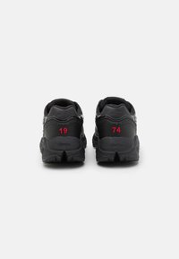 Black athletic shoes with textured leather upper, featuring red numbers "19" and "74" on the back and a rugged outsole for traction.