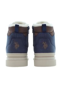 Marinblå och bruna vinterkängor med krämfärgad fleecefoder, beige sulor, sidodragkedjor, dragklämmor och polo-spelare logotyper på hälarna.