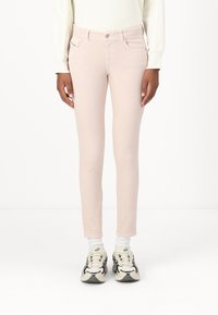 Jeans skinny de mezclilla rosa claro con un diseño clásico de cinco bolsillos, que presentan costuras sutiles y un cierre frontal con botón. Combinados con zapatillas.