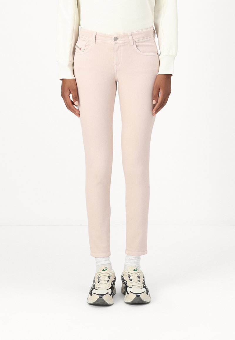 Jeans skinny de mezclilla rosa claro con un diseño clásico de cinco bolsillos, que presentan costuras sutiles y un cierre frontal con botón. Combinados con zapatillas.