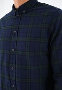 Chemise à carreaux bleu marine et vert foncé avec boutons et col boutonné portée sur la partie supérieure du torse.