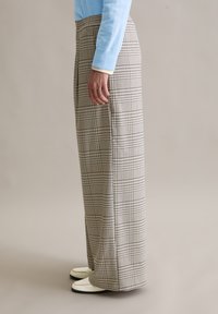 Wijd uitlopende broek in een beige ruitpatroon met zwarte en blauwe lijnen. Gemaakt van een gestructureerde stof, voorzien van een hoge tailleband en zijzakken.