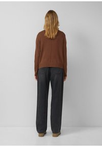 Brązowy sweter z dzianiny o luźnym kroju, z prążkowanym wykończeniem na dole, zestawiony z ciemnoszarymi, szerokimi spodniami z wysokim stanem. Gładka faktura, casualowy design.