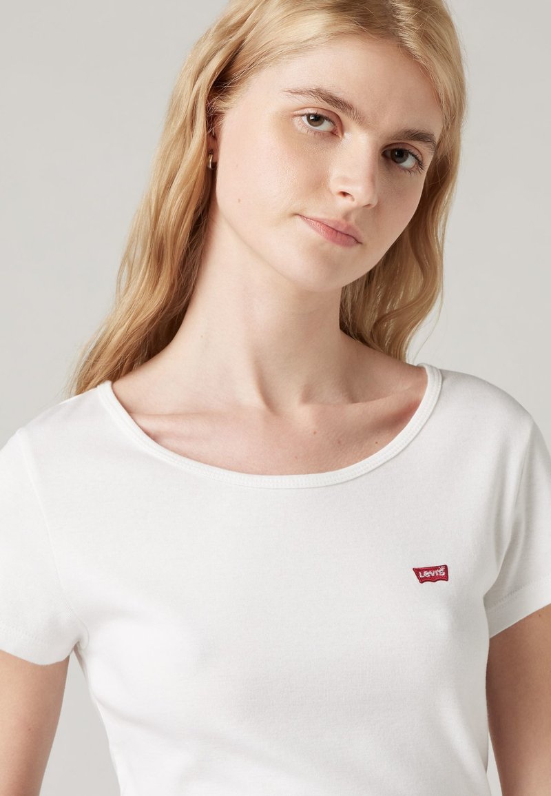 Camiseta de algodón blanca con mangas cortas, escote redondo y un pequeño logo rojo de Levi's en el pecho. Textura suave, diseño informal.