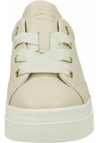 Beżowy skórzany trampek z płaskimi bawełnianymi sznurowadłami, złotymi oczkami i białą gumową podeszwą. Charakteryzuje się minimalistycznym designem i subtelnym brandingiem.