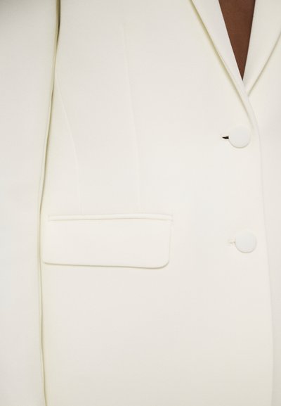 Blazer bianco con una texture liscia, revers a punte, due bottoni e una tasca a filetto sul lato sinistro. Vestibilità sartoriale con linee pulite.