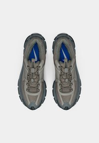 Nike pārgājienu apavi pelēkā un melnā krāsā, ar teksturētu augšdaļu, pastiprinātu purngalu un zilu akcentu uz zoles, ar drošu aizsaitēšanas sistēmu.