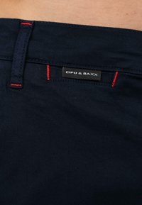 Primo piano della cintura dei pantaloni neri con cuciture rosse e un'etichetta del marchio "Cipo & Baxx".