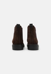 Barna velúr bokacsizmák texturált felülettel, fekete bőr részletekkel és tartós gumitalppal. Slip-on kialakítás rugalmas oldalakkal.