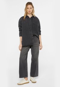 Oversized dark gray denim shirt with a chest pocket, worn with matching wide-leg dark jeans and beige sneakers with a rubber sole.