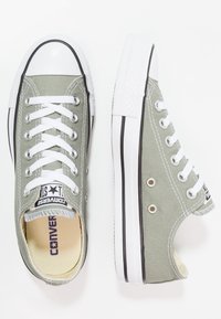 Hellgrüne Leinensneaker mit weißen Schnürsenkeln, Gummizähnen, schwarzem Rand und Logo auf der Zunge. Mit Ösen und strukturiertem Sohlenrand.