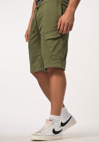 Shorts cargo vert olive avec taille élastique, poches latérales, design mi-cuisse, accompagnés de chaussures blanches avec un logo Nike en noir.