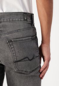 Grå denim jeans med lav midje, detaljerte baklomme-sømmer og en logolapp på livet. Glatt tekstur.