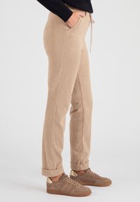 Beige corduroy broek met rechte snit, elastische tailleband en trekkoord. Voorzien van zijzakken en opgerolde pijpen, gecombineerd met bruine sneakers.
