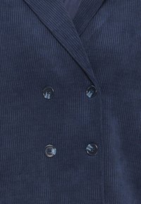Blazer en velours côtelé bleu marine avec un design croisé, un tissu texturé et deux boutons avec des motifs rayés subtils.