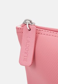 Pochette en nylon rose avec une surface texturée, quincaillerie en argent et tirette de fermeture éclaire rose assortie avec le nom de la marque en relief.