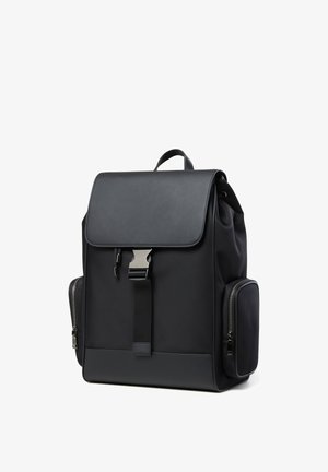 Schwarzer rechteckiger Rucksack mit oberer Klappe, Metallverschluss, vorderem Riemen, seitlichen Reißverschlusstaschen und Tragegriff auf weißem Hintergrund.