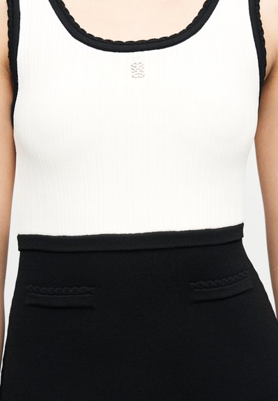 Γυναίκα που φοράει λευκό αμάνικο τοπ με μαύρο περίγραμμα και μαύρη ψηλόμεση φούστα με υφασμένα σχέδια στις τσέπες.