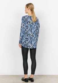 T-shirt à manches longues arborant un motif floral bleu sur un fond clair, associé à un legging noir ajusté et des chaussures noires.