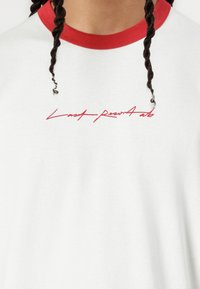 White t-shirt with a red ribbed collar. Features red cursive text "Last present" on the front. Slightly textured fabric, casual fit.