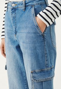 Pantalones cargo de mezclilla azul claro con bolsillos laterales, con una cintura alta y detalles de costura visibles. Parte superior estampada con rayas en blanco y negro.