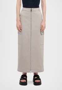 En lang, beige nederdel lavet af bomuld med en frontlynlås og to sidelommer. Båret med sorte plateau-sandaler med spænder.