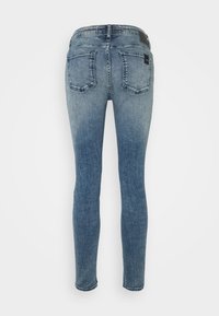 Vaqueros ajustados en denim azul claro, vistos desde la parte posterior, con dos bolsillos traseros y una etiqueta de marca en la cintura.