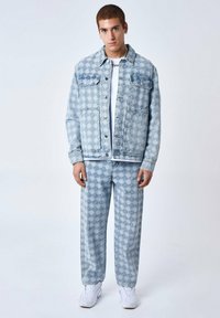 Veste en denim bleu clair et pantalons assortis avec un motif géométrique, de coupe décontractée et deux poches avant. T-shirt blanc en dessous.