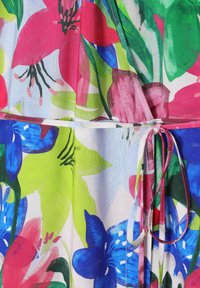 Bloemjurk met een levendig patroon van roze, blauwe en groene bloemen, gemaakt van een lichte stof met een strikdetail bij de taille.