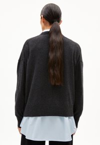 Hematietgrijze oversized trui met geribbelde manchetten en zoom, gelaagd over een lichtblauw shirt, met een ontspannen pasvorm en een gladde textuur.