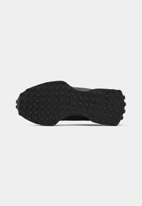 Semelle de chaussure noire avec des motifs circulaires de la bande de roulement uniformément espacés sur toute la surface, présentée sur un fond clair uni.