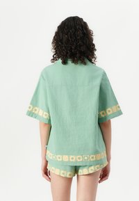 Groene linnen set met korte mouwen en shorts, versierd met een gouden bloemenrand. Ontspannen pasvorm met een gestructureerd oppervlak.