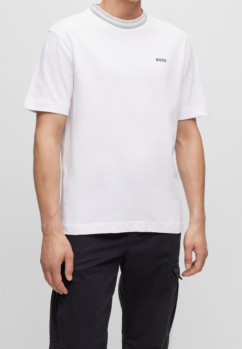 White cotton T-shirt with short sleeves, featuring a ribbed collar with gray accents and a small green "BOSS" logo on the left chest.