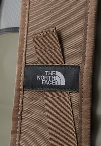 Brun rugletekstur med sømmer, med et svart merke med hvit tekst og logo fra The North Face.