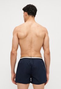 Navy swim shorts featuring an elastic waistband with a silver accent. Made of lightweight material with a smooth texture and no visible patterns.