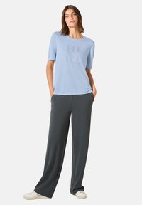 Camisa de manga corta azul claro con diseño de texto, combinada con pantalones oscuros de corte holgado en gris y zapatillas blancas, con un ajuste relajado.