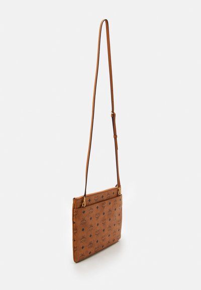 Sac en cuir marron à portée traversée avec une sangle réglable, recouvert de motifs en répétition du logo noir MCM et de motifs en diamant, présenté en suspension.