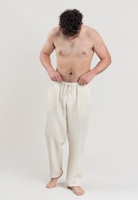 Pantalons à cordon de serrage texturés, de couleur beige clair, avec une coupe ample, dotés de poches latérales et d'une cheville décontractée. Le tissu semble respirant et doux.