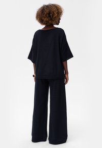 Zwarte katoenen oversized top met brede mouwen, gecombineerd met losse zwarte broek. Zachte textuur en minimalistisch ontwerp, geen zichtbare patronen.