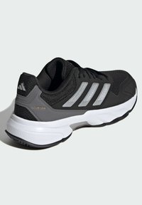 Zapato deportivo negro con parte superior de malla y acentos plateados, una entresuela blanca acolchada y una suela de goma texturizada para mayor agarre.