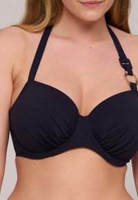 Top bikini blu navy con coppe morbide, arricciatura al centro e spalline regolabili con un dettaglio a forma di anello color oro. Texture liscia.