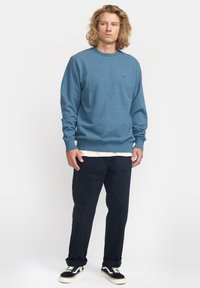 Blauwe crewneck sweatshirt van zachte stof, met een kleine geborduurde roos. Gecombineerd met donkerblauwe broek en zwart-witte sneakers.
