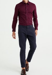 Kastanjefärgad skjorta med lång ärm, tillsammans med marinblå byxor. Bruna loafers fulländar outfiten. Slät textur och smal passform.