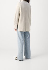 Gehaakte crèmekleurige trui met een hoge kraag, een ontspannen pasvorm, geribbelde textuur en lange mouwen; gecombineerd met lichtblauwe wijde jeans.