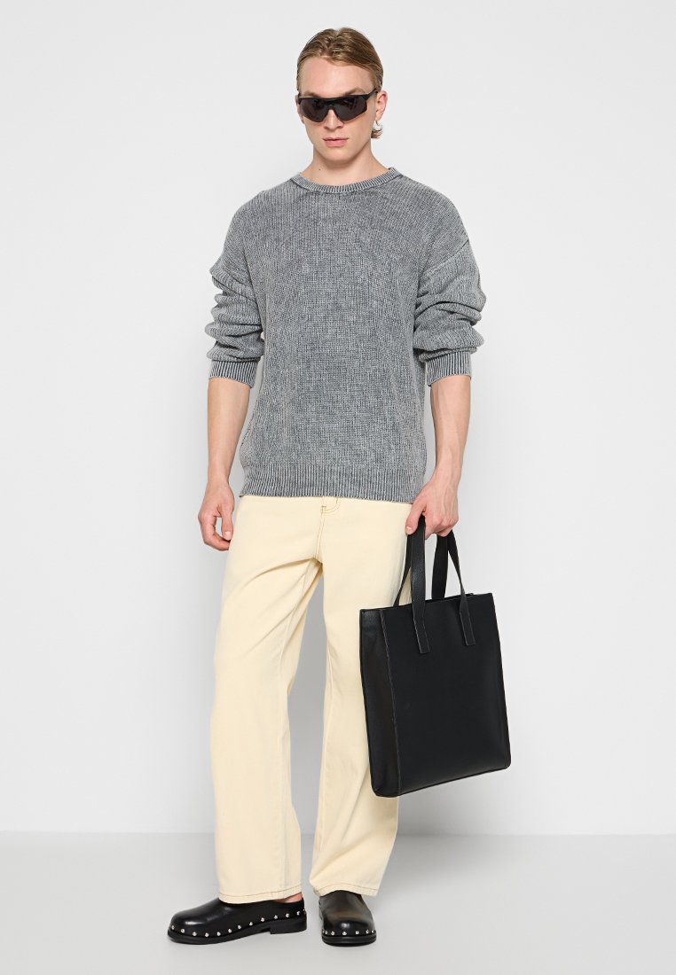 Grijze gebreide trui, crèmekleurige wijde broek, zwart leren tote bag en zwarte instappers met studs. Strak ontwerp en minimale accenten.