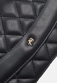 Sac en cuir noir matelassé avec une texture lisse, une couture détaillée et un accent logo doré sur la sangle.