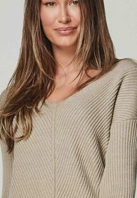 Beige gerippter Strickpullover mit V-Ausschnitt, weiten Ärmeln und strukturierter Stoffqualität, mit einer zentralen Naht auf der Vorderseite.